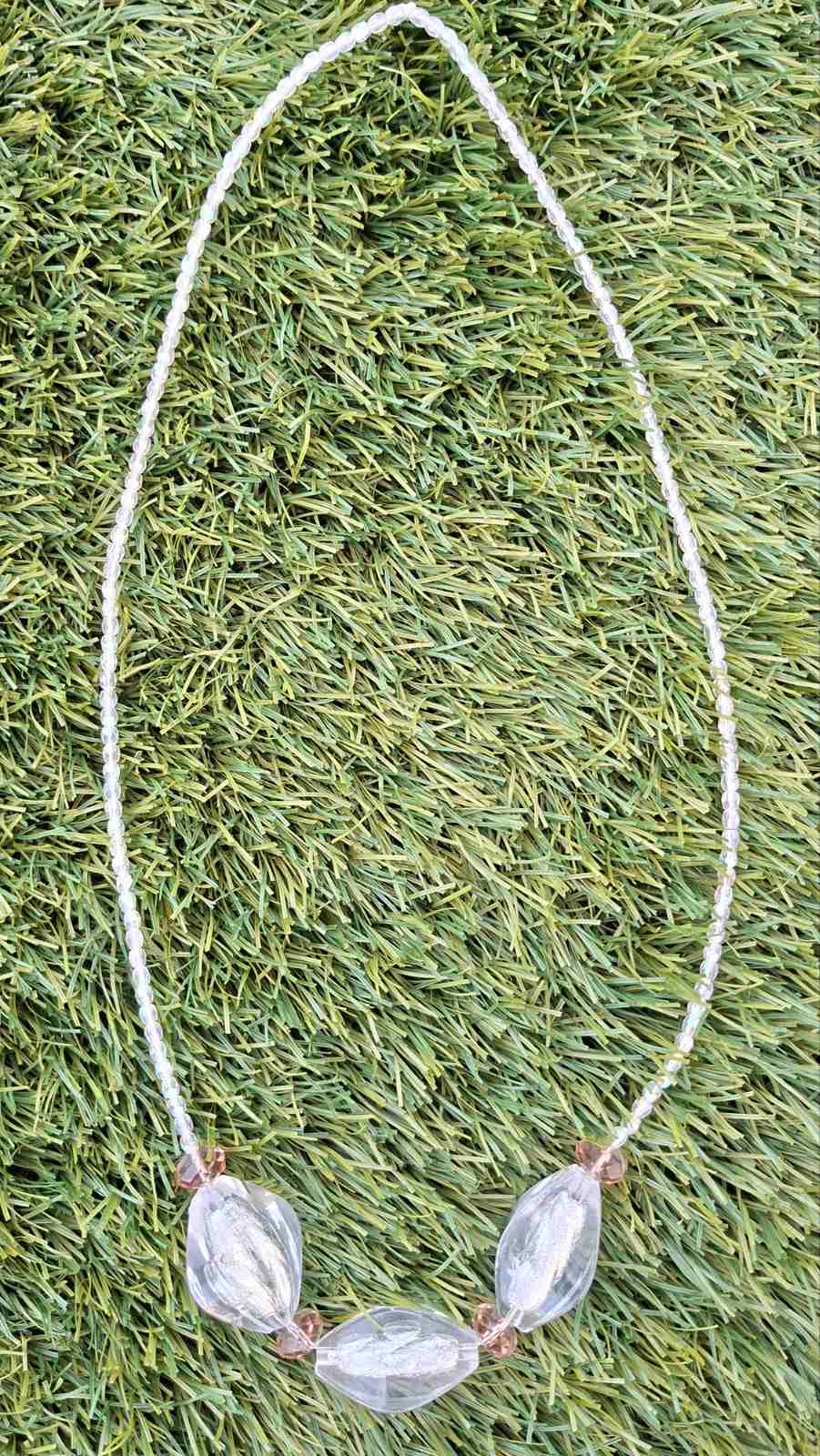 Triple stone crystal necklace laid flat on green grass