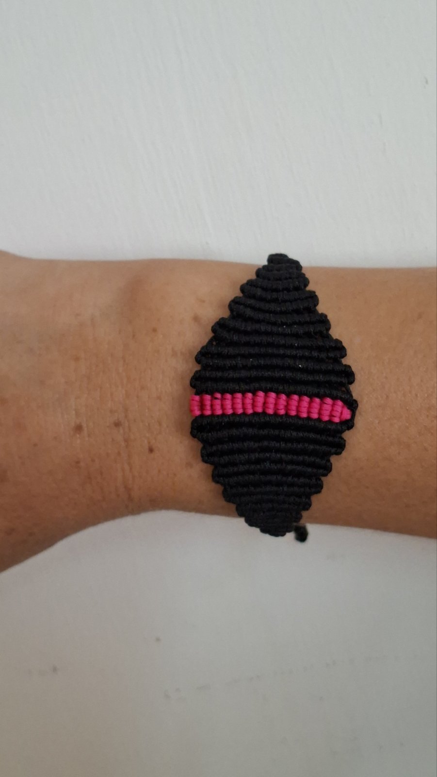 Handmade black macramé bracelet with pink accent stripe worn on wrist - side view