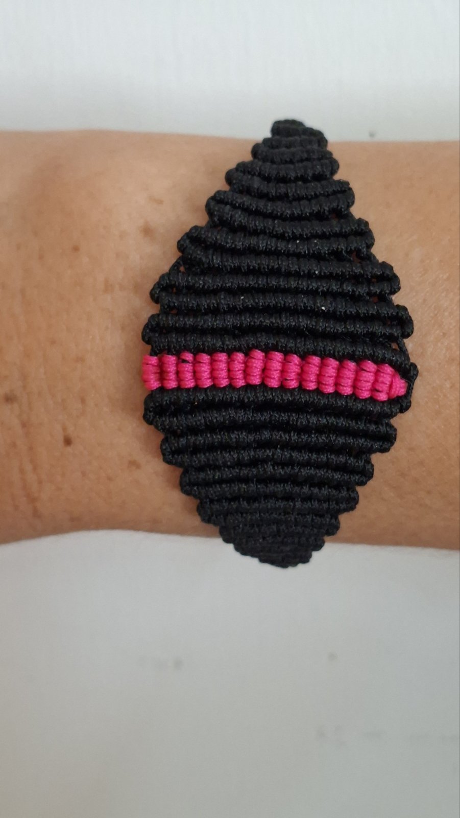 Handmade black macramé bracelet with pink accent stripe worn on wrist - front view