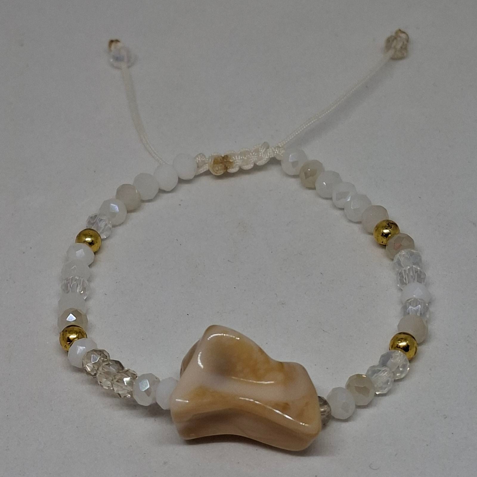 A beaded bracelet featuring a large, organic-shaped cream and tan stone bead at the center, surrounded by white round beads, clear faceted beads, and small metallic gold spacer beads, on a light gray background.