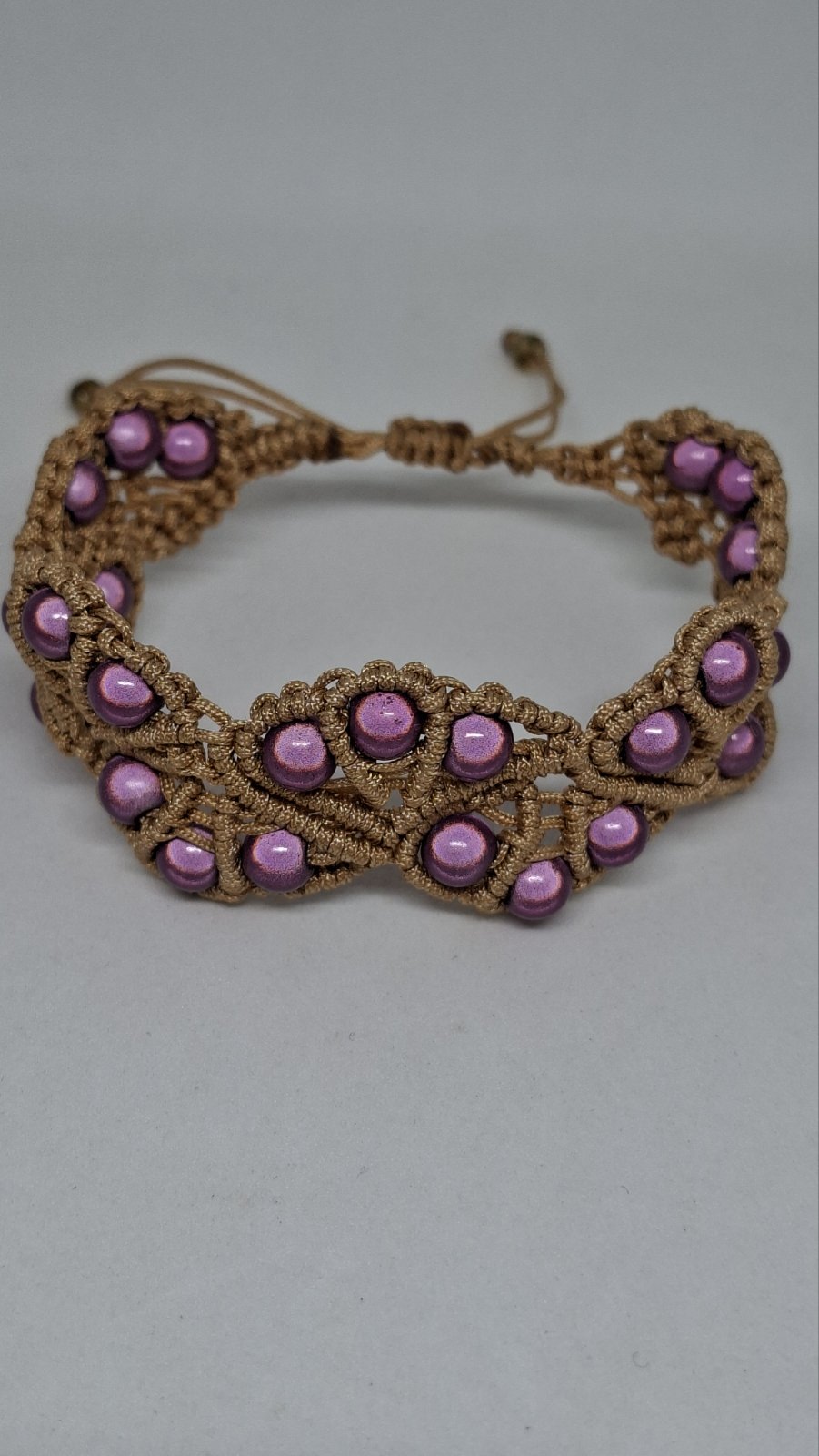 Macramé pearl bracelet in mauve laid flat on white background