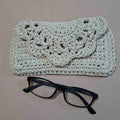 Handmade crochet glasses case with floral flap beside black glasses