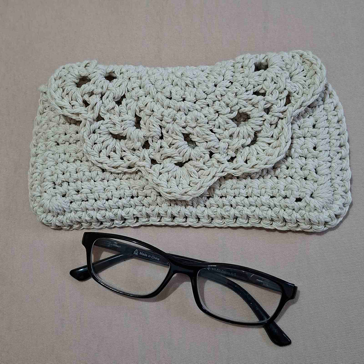 Handmade crochet glasses case with floral flap beside black glasses