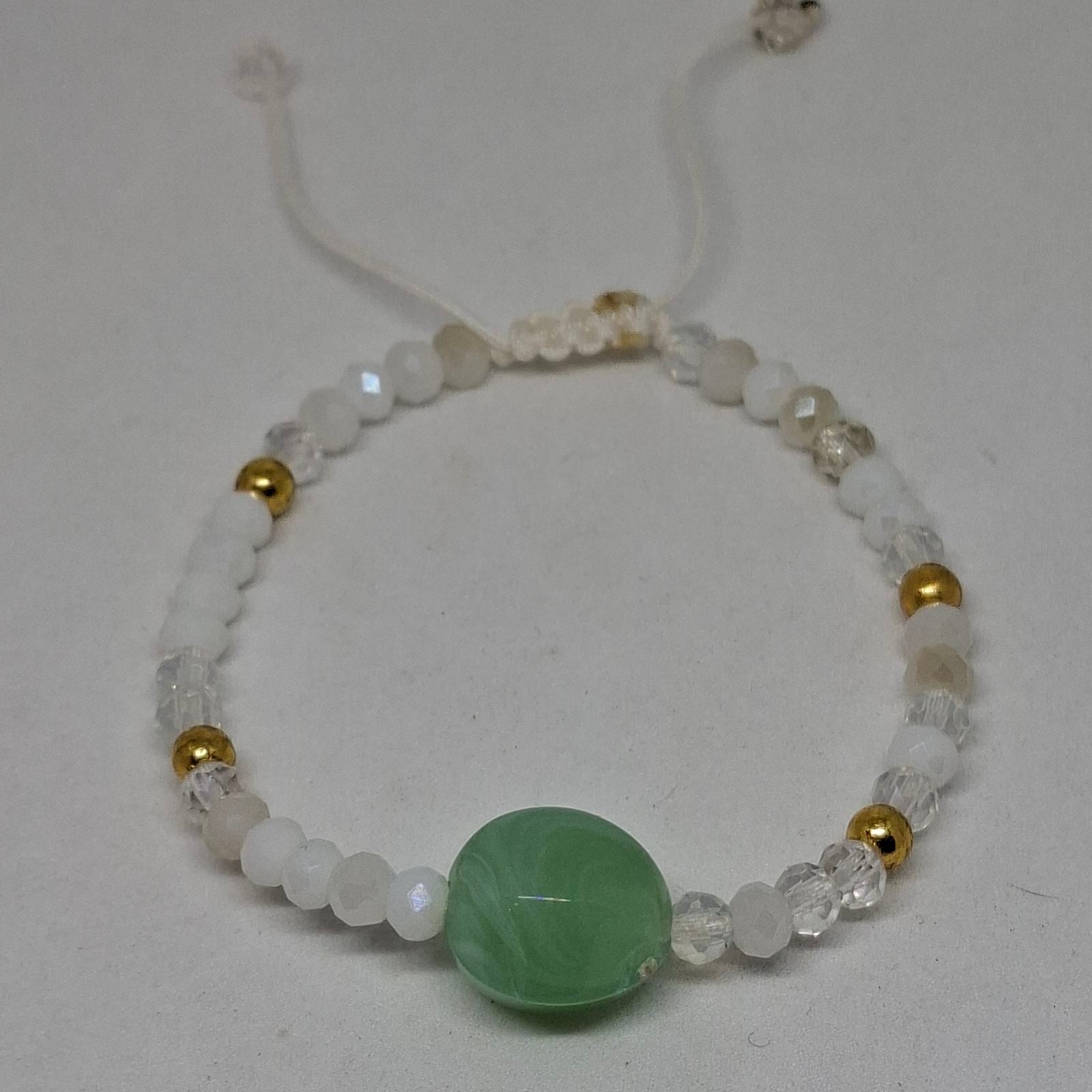 A beaded bracelet featuring a large central green stone bead, surrounded by white and clear faceted beads, with small gold spacer beads, on a light gray background.