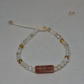 A beaded bracelet featuring a central rectangular brown stone bead, surrounded by clear faceted beads, white beads, and small metallic gold beads, with a white adjustable cord.