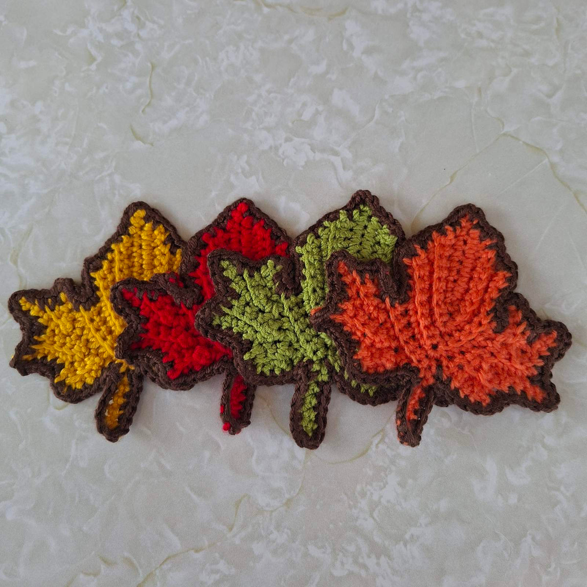 Four crochet leaf coasters arranged in an overlapping row