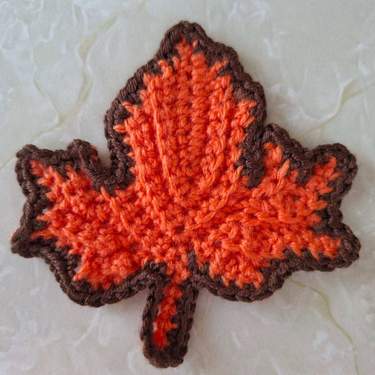 Orange crochet leaf coaster with brown edging