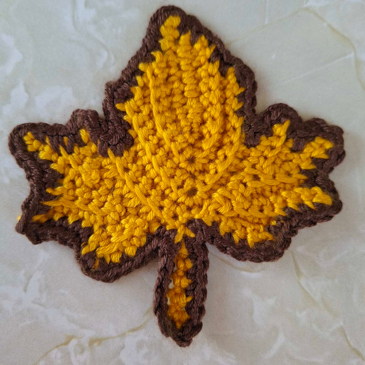 Mustard yellow crochet leaf coaster with brown edging
