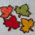 Set of four crochet autumn leaf coasters in orange, green, red and mustard yellow with brown edging
